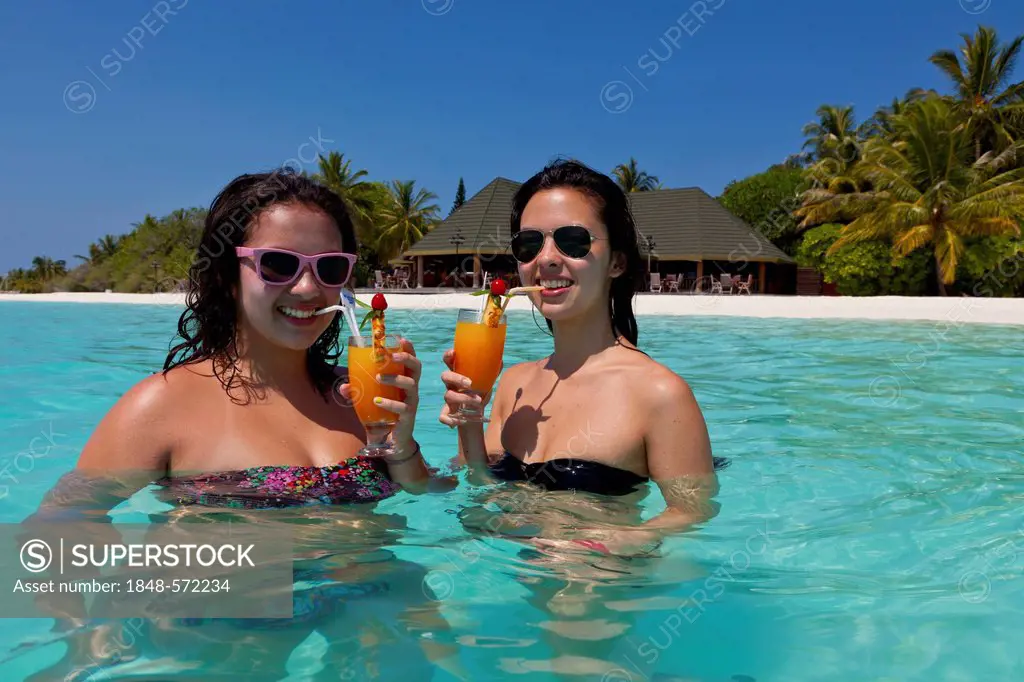 Two girls, about 14 and 18 years old, wearing sunglasses, drinking cocktails in a turquoise-coloured lagoon in the sea in front of the Paradise Island...