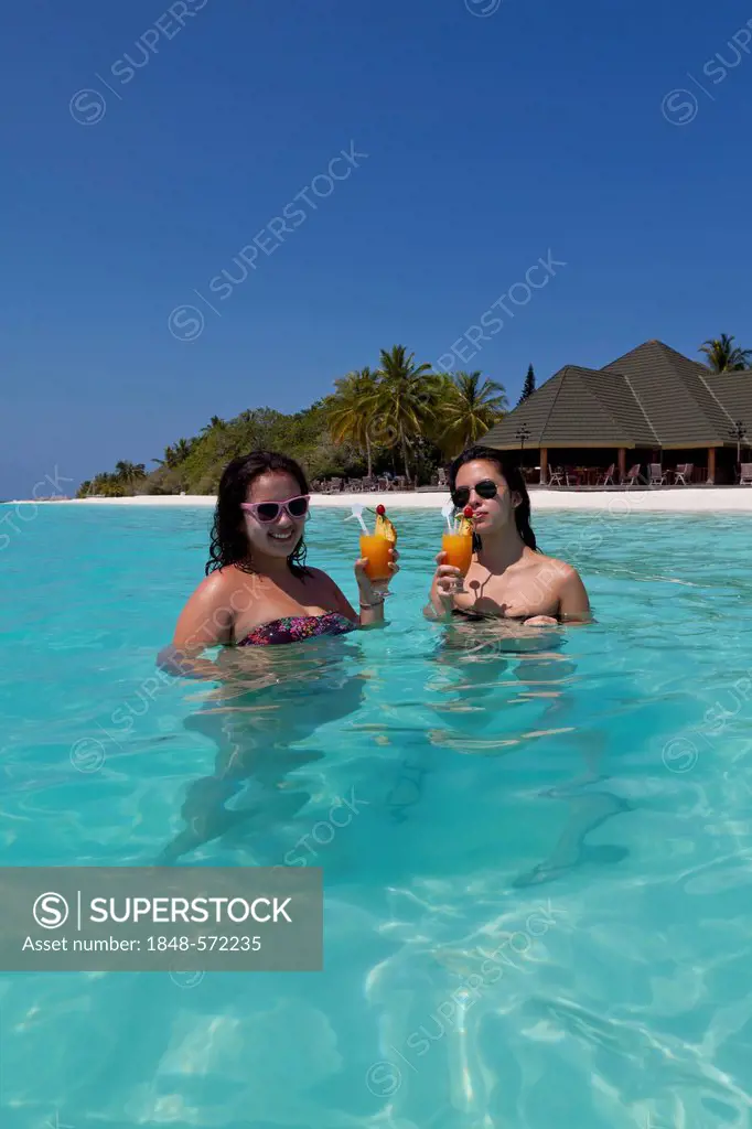 Two girls, about 14 and 18 years old, wearing sunglasses, drinking cocktails in a turquoise-coloured lagoon in the sea in front of the Paradise Island...