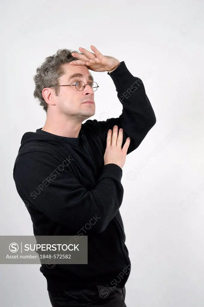 Young man with glasses holding his hand to his forehead and looking into the distance