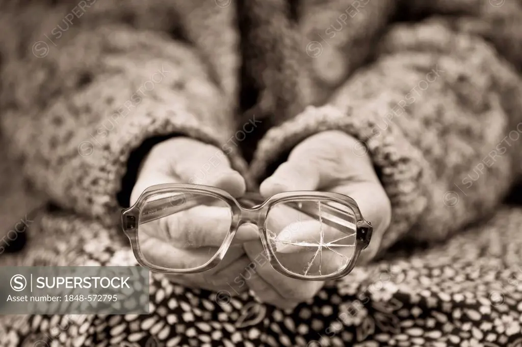 Hands of an old woman holding old broken glasses, sepia processing