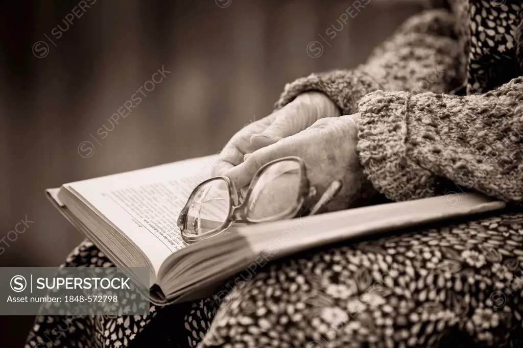 Hands of an old woman holding old broken glasses on a book, sepia processing