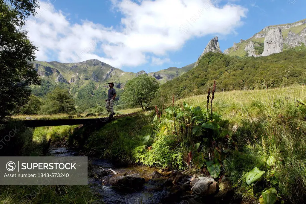 Hiker crossing a footbridge, Chaudefour Valley natural reserve, Parc Naturel Regional des Volcans d'Auvergne, Auvergne Volcanoes Regional Nature Park,...