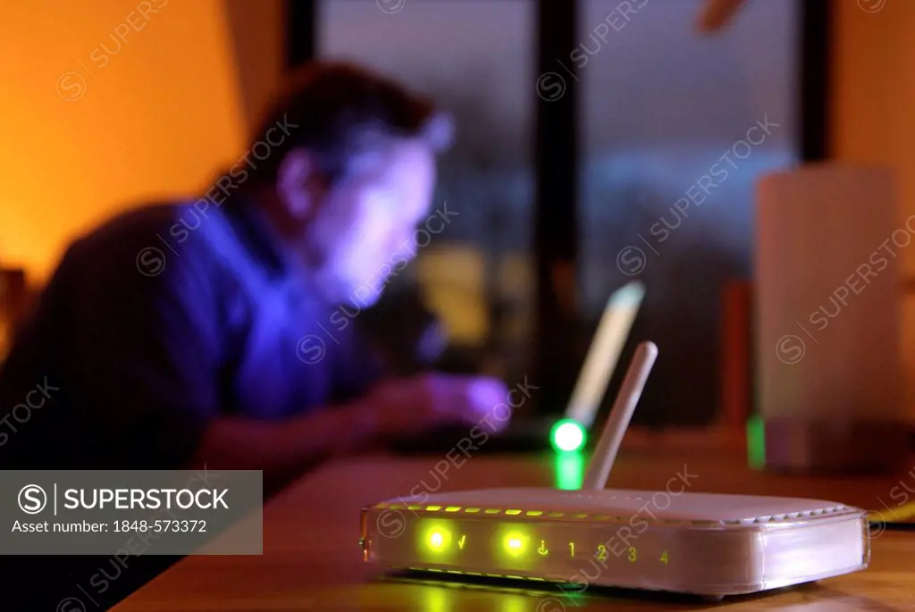Router for distributing an incoming broadband connection via Wi-Fi, wireless to computers, in front of a man using a computer in an apartment