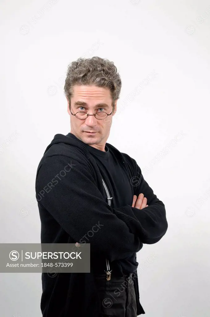 Young man with folded arms looks confidently and challengingly above his glasses