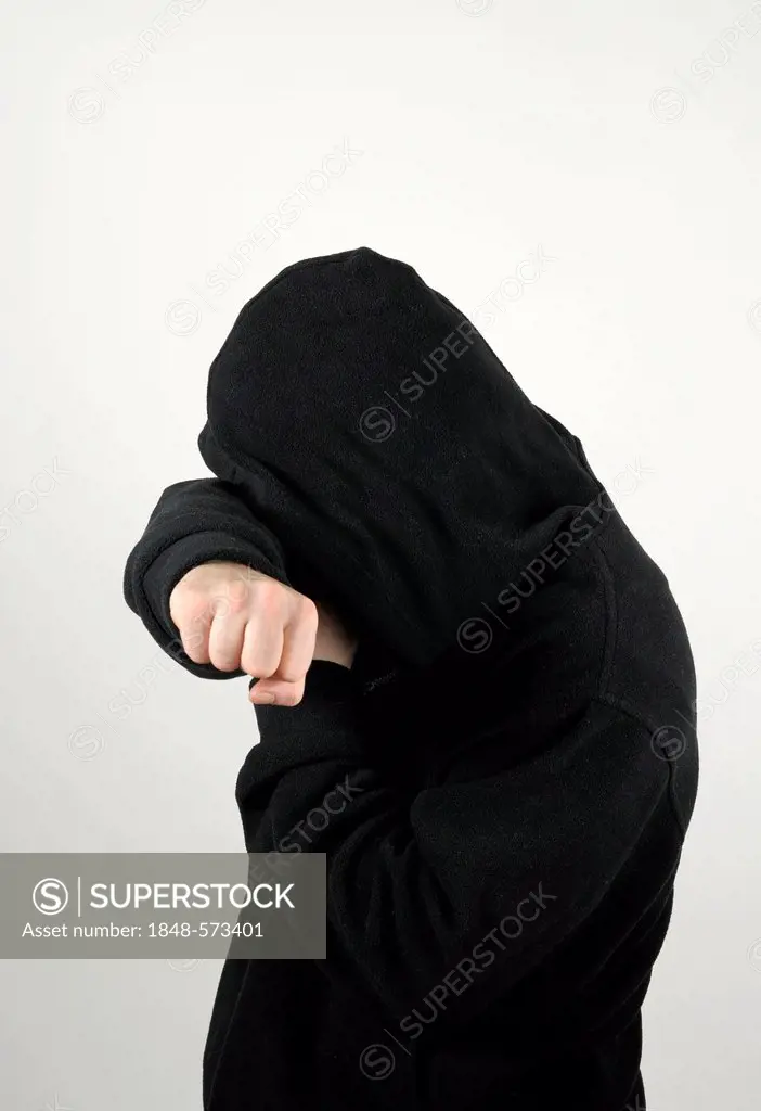 Young man wearing a black hooded shirt holding his arm protectively over his eyes obscuring his face