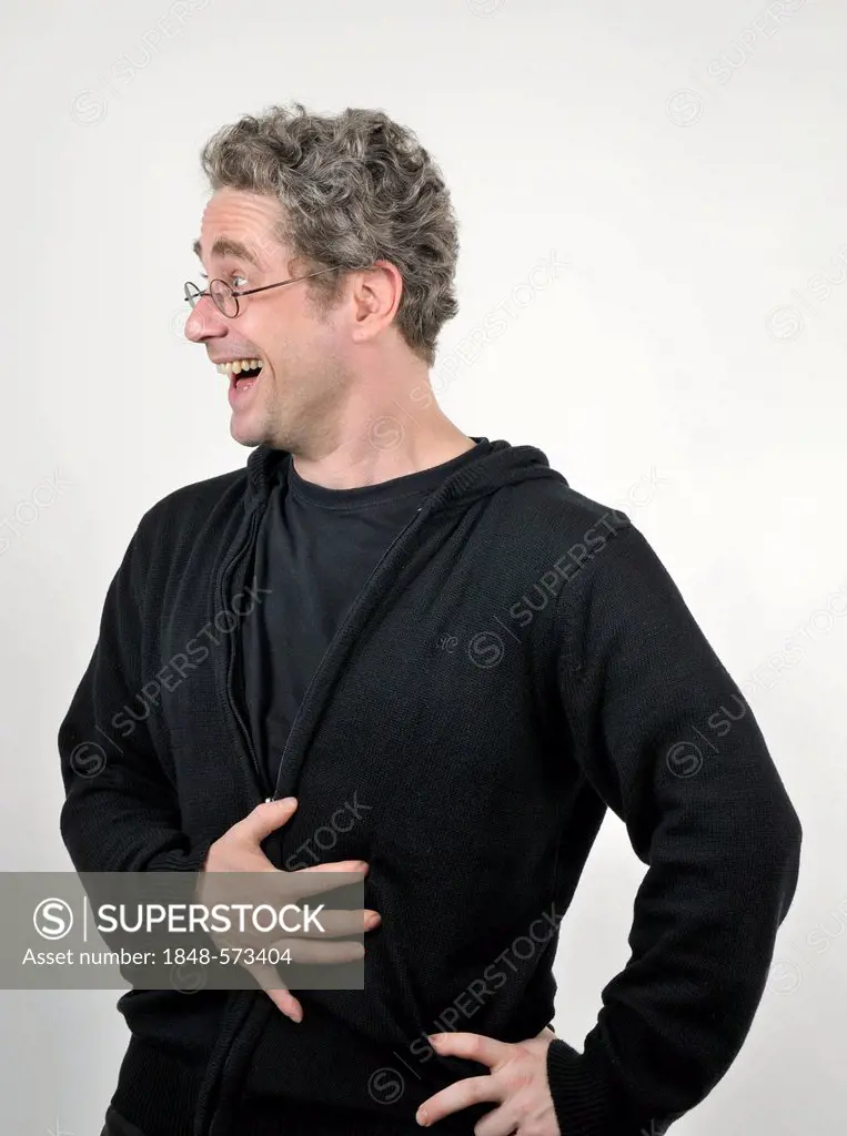 Young man with glasses laughing heartily, one hand on his abdomen