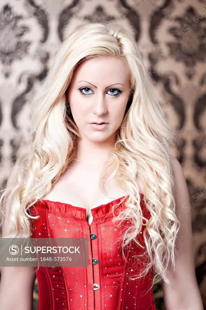 Blonde woman in a red corset in front of a baroque wallpaper