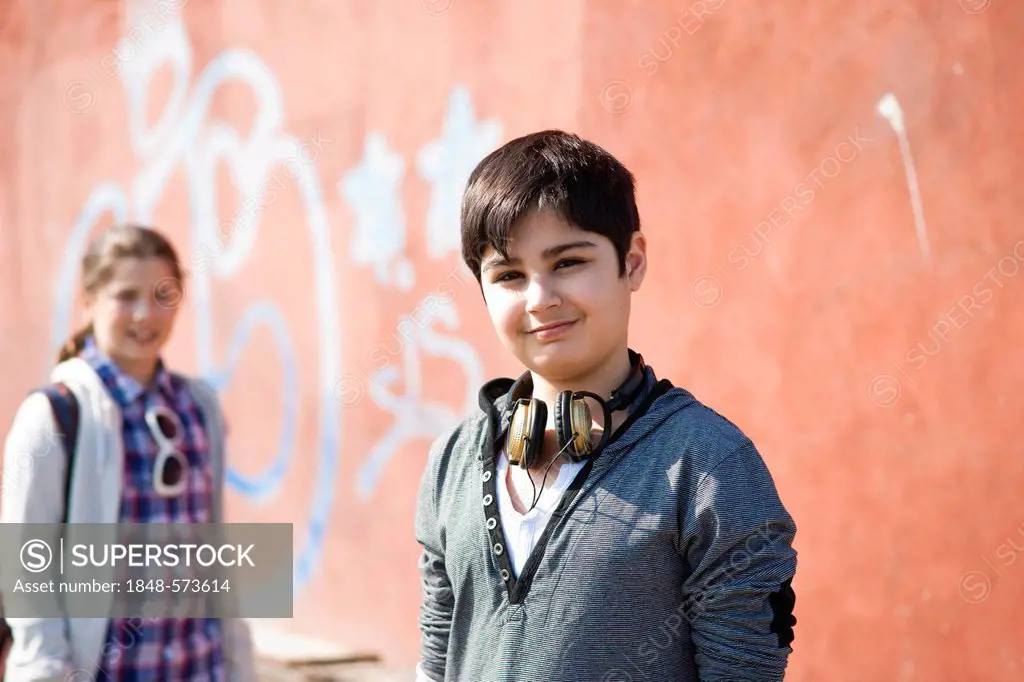 Boy with headphones and a girl in front of a wall with graffiti