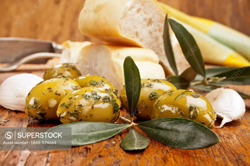 Green olives with an olive branch, bread, garlic and cutlery at the back