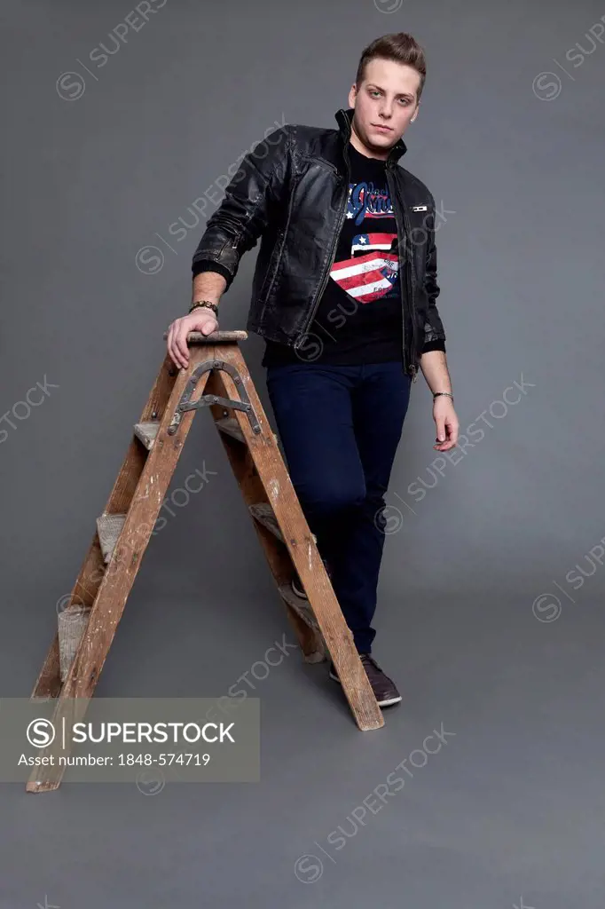 Young man wearing a leather jacket and jeans, standing next to an old wooden ladder