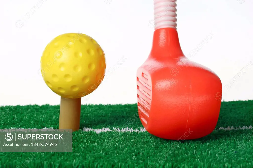Toy plastic golf equipment, golf club and a golf ball on a hitting mat with a tee and artificial turf
