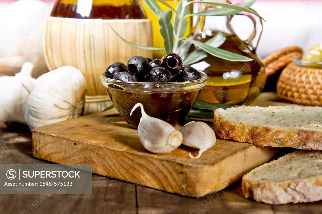 Olives, garlic, olive oil and fresh bread on a wooden table