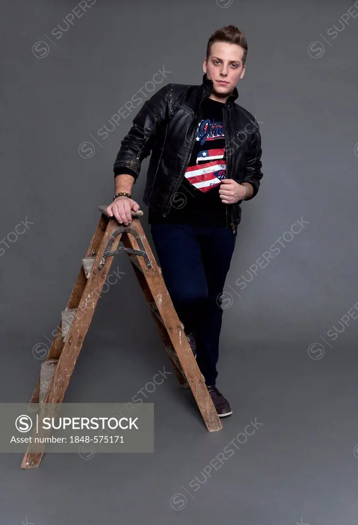 Young man wearing a leather jacket and jeans, standing next to an old wooden ladder