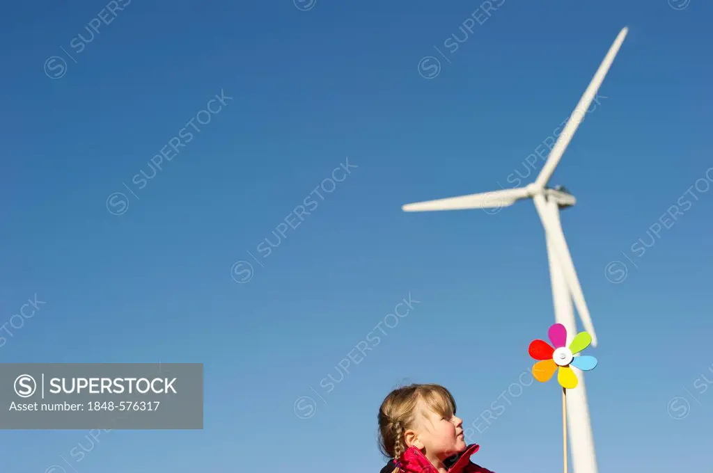 Girl holding a toy windmill in front of a wind turbine, near Freiburg in Breisgau, Black Forest, Baden-Wuerttemberg, Germany, Europe
