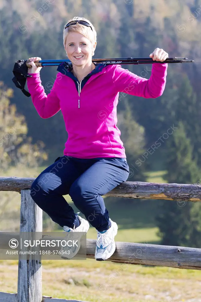 Young woman with Nordic Walking poles sitting on a fence, Waidhofen Ybbs, Lower Austria, Mostviertel, Austria, Europe
