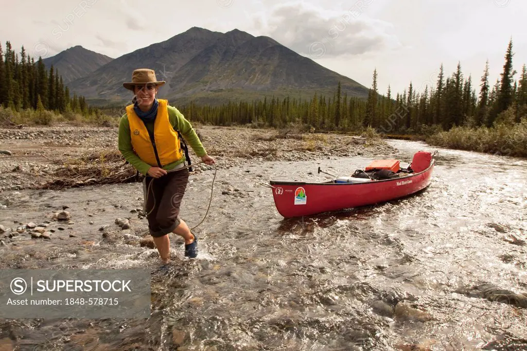 Young woman lining, wading, pushing, pulling a canoe in shallow water, Wind River, Peel Watershed, Northern Mackenzie Mountains behind, Yukon Territor...
