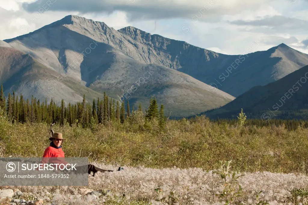 Young woman relaxing, enjoying evening light, sitting in the grass, Cotton Grass, Peel Watershed, Northern Mackenzie Mountains behind, Wind River, Yuk...