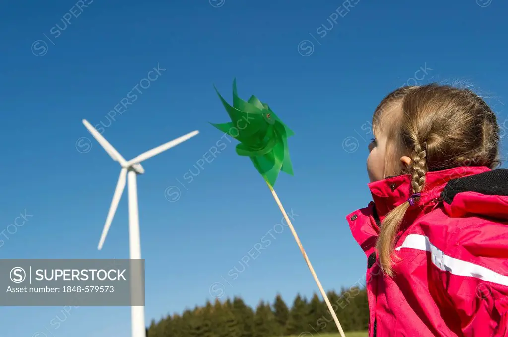 Girl holding a green pinwheel in front of a wind turbine, near Freiburg in Breisgau, Black Forest, Baden-Wuerttemberg, Germany, Europe