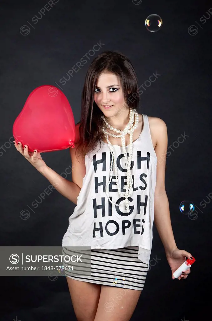 Young woman, wearing a top with the words High heels, high hopes, with bubbles and a heart-shaped balloon