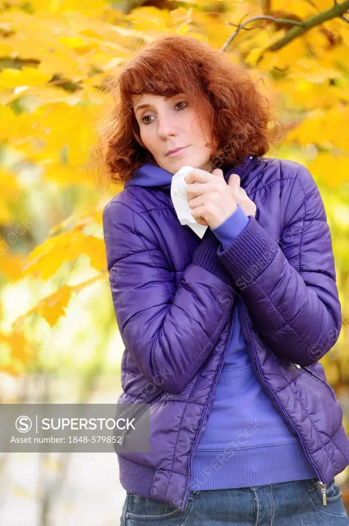 Woman with a cold holding a handkerchief in autumnal surroundings