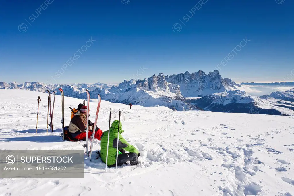 Ski tourers taking a break on the summit of Mt Uribrutto, above Passo Valles, Dolomites, Pale di San Martino mountains and the Passo Rolle in the back...