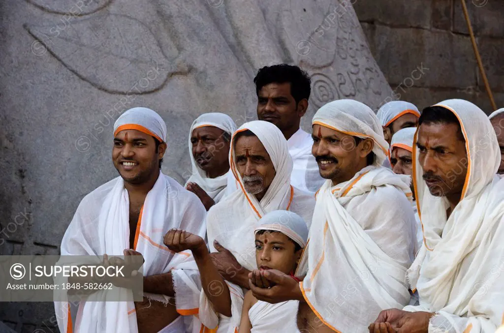 A group of Jain pilgrims is reciting religious texts at the feet of the gigantic statue of Gomateshwara in Sravanabelagola, Karnataka, India, Asia