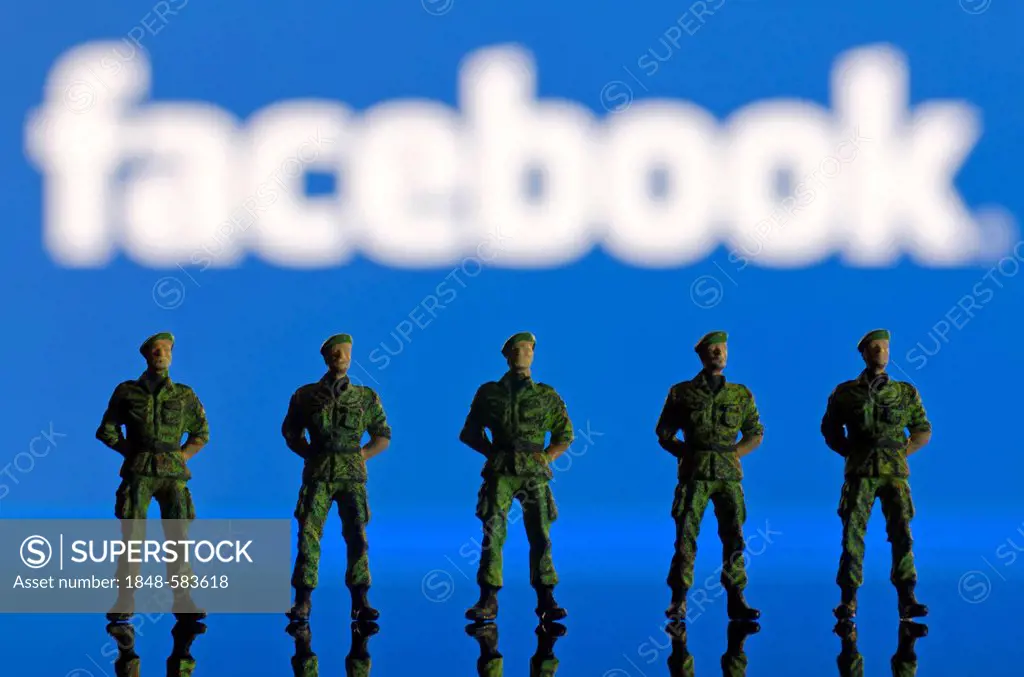 A row of soldiers, miniature figures standing in front of a blurred Facebook logo, symbolic image