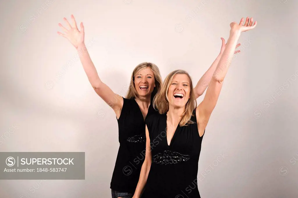 Twin sisters cheering with arms raised