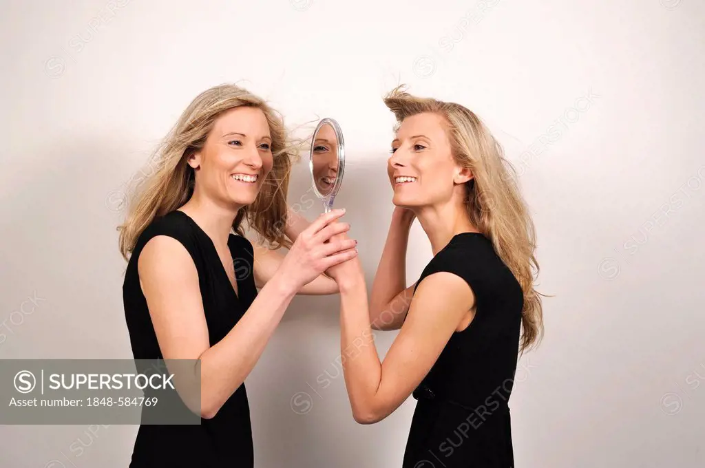Twin sisters looking from both sides into a hand mirror