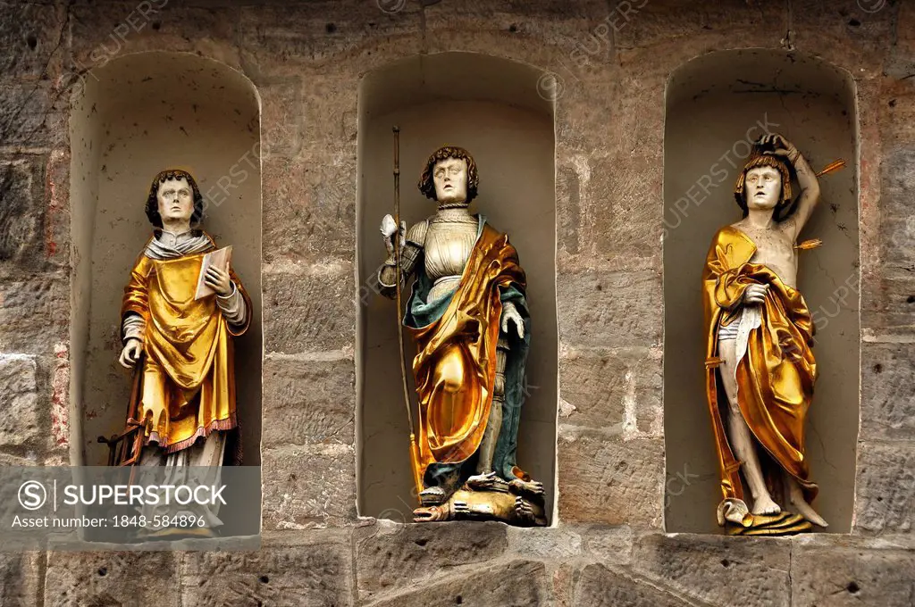 Three coloured statues of saints, from left, St. Lawrence holding a gridiron, St. George and the Dragon, St. Michael with the arrows in niches in the ...