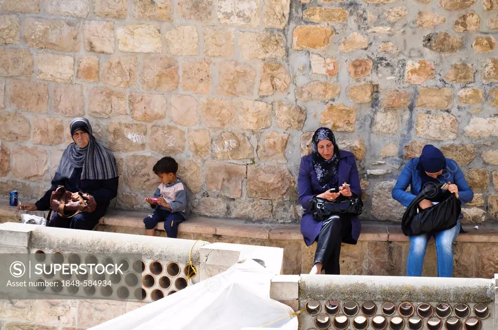 Veiled women smoking cigarettes and cell phones and a boy sitting on the city wall, Jerusalem, Israel, Middle East, Southwest Asia