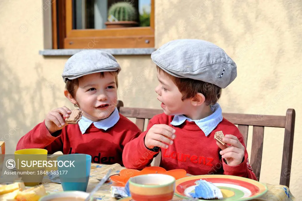 Twin boys, 4, wearing flat caps, sitting and eating at a table