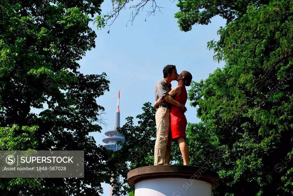 Kissing couple under trees, sculpture on an advertising column in the back the Rheinturm telecommunications tower, Duesseldorf, North Rhine-Westphalia...