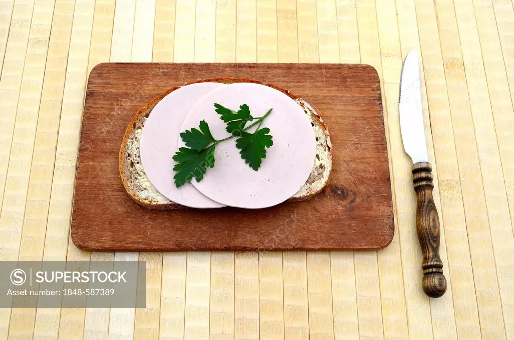 Bread with ham sausage and parsley, wooden board, breakfast knife with wooden handle