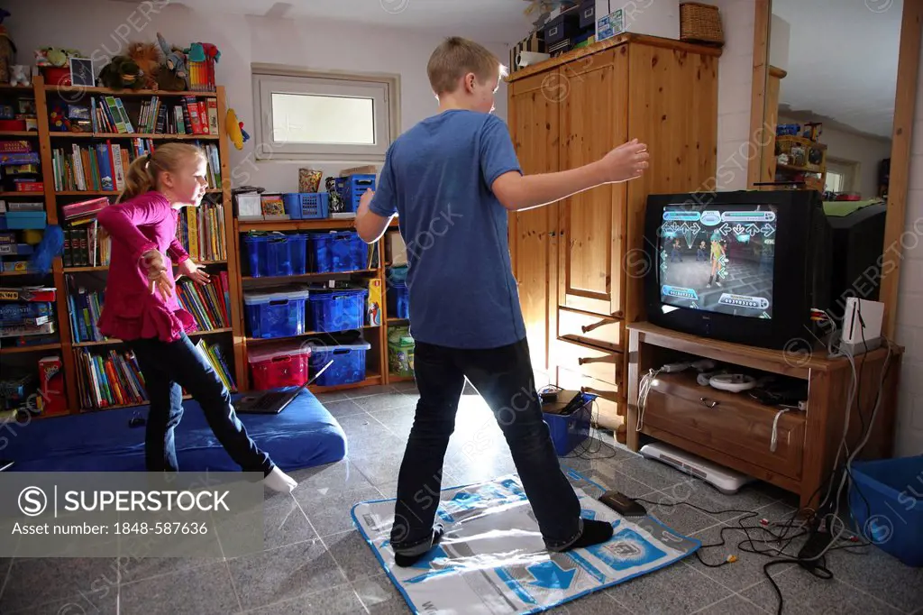 Siblings, a boy, 12 years old, and a girl, 10 years old, playing a dance game on a Wii games console in their room together