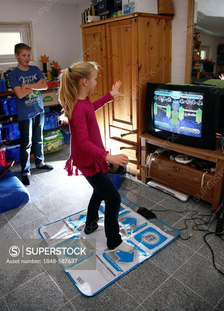 Siblings, a boy, 12 years old, and a girl, 10 years old, playing a dance game on a Wii games console in their room together