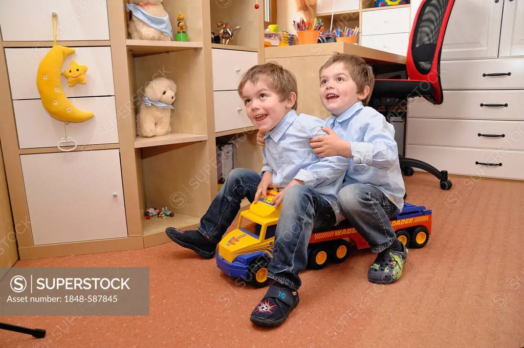 Twin boys, 4, riding together on a toy truck