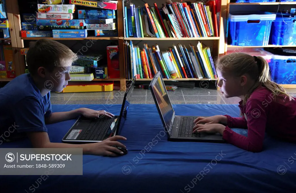 Siblings, a boy, 12 years, and a girl, 10 years, playing computer games on two laptops in their room