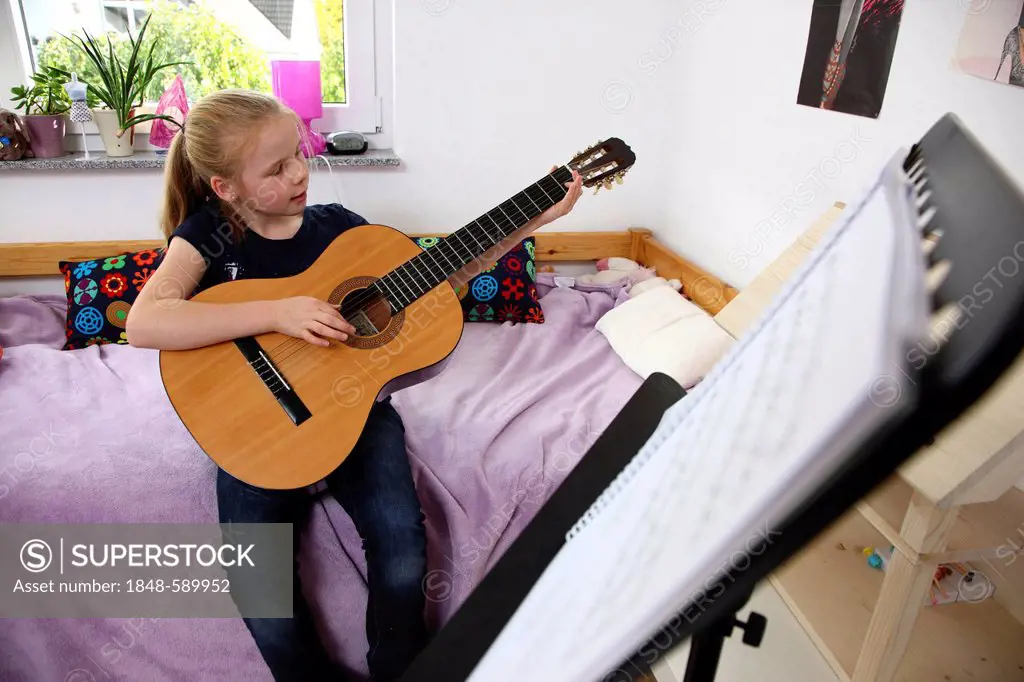 Girl, 10 years, practising to play the guitar in her room