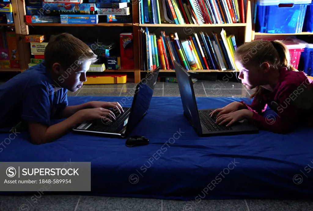 Siblings, a boy, 12 years old, and a girl, 10 years old, playing computer games on laptop computers in their room