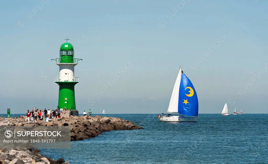 Sailing boat passing the lighthouse at the harbour entrance to Warnemuende seaside resort, Mecklenburg-Western Pomerania, Germany, Europe