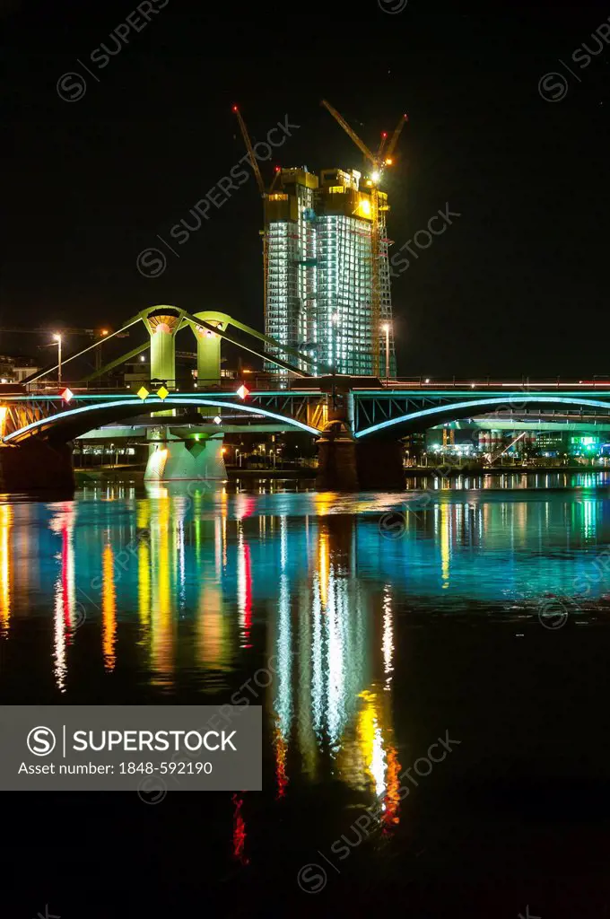 Brightly illuminated Floesser Bridge at night, the illuminated new development of the European Central Bank, ECB, at back, mirrored in the Main river,...