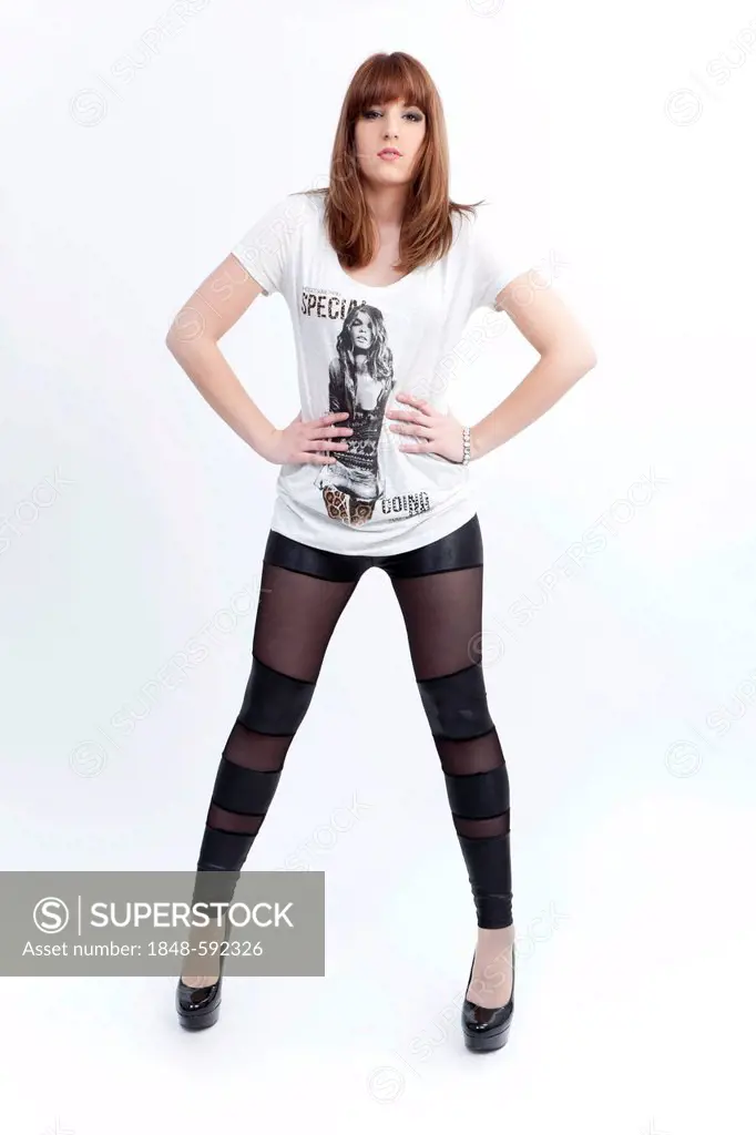 Young woman in a white top, dark leggings and high heels, posing with self-confidence