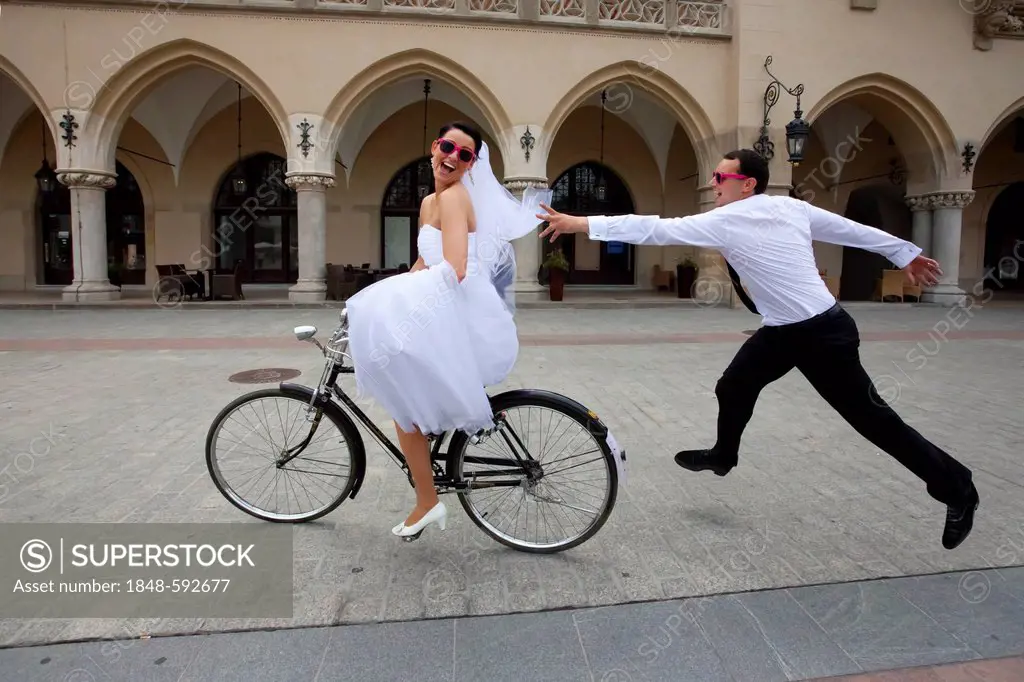 Bride riding a bicycle, riding away from groom