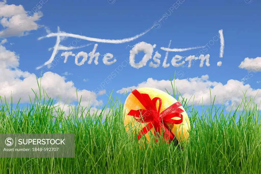 Easter egg with a bow lying in the grass, lettering Frohe Ostern, German for Happy Easter