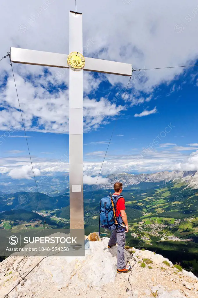 Mountain climber at the summit cross on the Latemar Crossing climbing route, Latemarspitz Mountain, in front of the Rosengarten Group, Dolomites, Alto...
