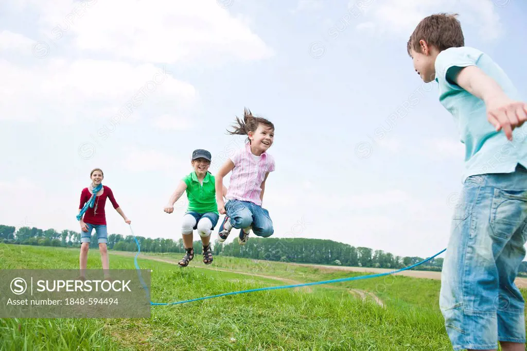 Four friends, three girls and a boy jumping ropes in a meadow