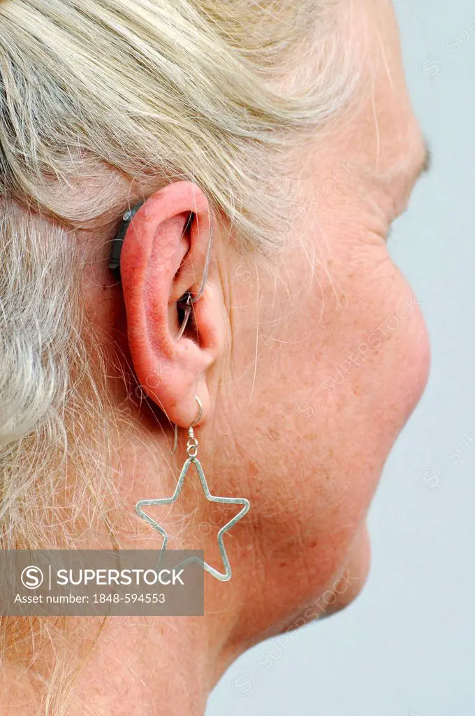 Modern small hearing aid behind the ear of a woman, 55 - 60 years, earring, hardness of hearing