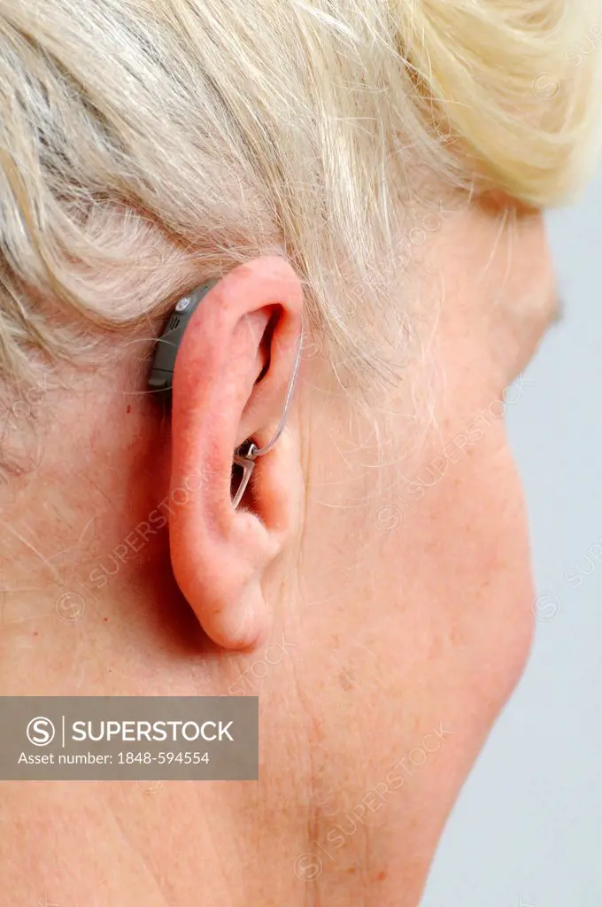 Modern small hearing aid behind the ear of a woman, 55 - 60 years, hardness of hearing