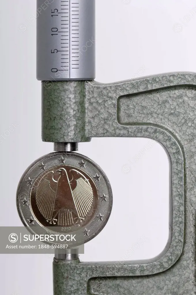 Two-euro coin in micrometer gauge, symbolic image for the euro under pressure